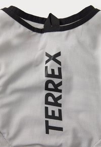 White mesh athletic shirt with a round neckline, featuring a large black "TERREX" logo on one side and a black trim along the neck.