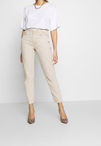 Beige högmidjade jeans med avsmalnad ben, matchat med en lös vit T-shirt och klackar med leopardmönster. Kedjehalsbandet accentuerar outfiten.