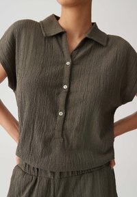 Short-sleeved, olive green blouse with a textured fabric. Features a classic collar and five button placket with round, light-colored buttons.