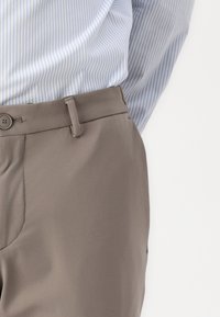 Lys blå stripete skjorte lagdelt over grå bukser. Buksene har knappelukking, glatt tekstur og et slim fit design.
