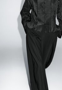 Camicia a righe bianche e nere con una vestibilità sartoriale, abbinata a pantaloni neri con una superficie liscia e una silhouette rilassata.