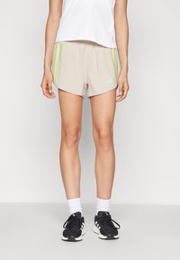 Pantalones cortos deportivos beige con rayas verdes, hechos de un tejido ligero. Presentan un logo de Adidas en azul y un corte relajado, con una longitud por encima de la rodilla.