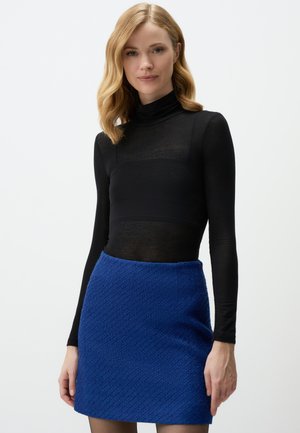 Zwarte lange mouwen turtleneck top, gecombineerd met een gestructureerde blauwe mini-rok. De top is doorschijnend, terwijl de rok een geweven patroon heeft.