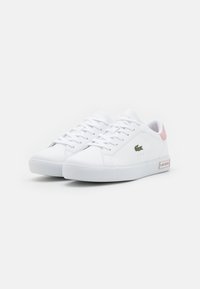 White sneaker with a smooth leather upper, pink accent on the heel, lace-up design, and green embroidered logo on the side. Rubber sole.