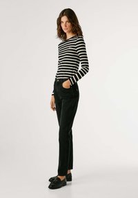 Svītrainā melnbaltā garām piedurknēm virsma, apvienota ar augstām melnām džinsām. Tērpā ir melni loafers un tam ir ikdienišķs piegriezums.