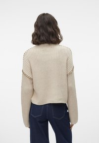 Beige strikkegenser med løs passform, ribbestruktur og senkede skuldre. Brukt sammen med mørk denim med detaljer på baksemen.