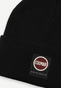 Svart stickad mössa med vikbar kant, prydd med en rund Colmar-logotyp i röd och vit på en svart lapp. Texturen är jämn och tyget är elastiskt.