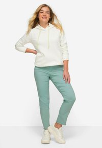 Sudadera blanca con cordón, combinada con pantalones verde menta. El conjunto presenta texturas suaves y zapatillas ligeras y casuales.