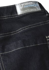 Jean en denim bleu foncé avec des coutures jaunes. Présente une étiquette métallique avec du texte et des coordonnées au niveau de la taille. Design classique.