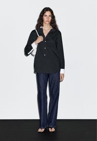 Black and white striped button-up shirt with a white collar, paired with dark blue wide-leg jeans and a white handbag. Flat sandals.