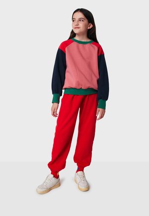 Color-blocked sweatshirt in pink, red, and navy with green accents, paired with red sweatpants. Features ribbed cuffs and casual fit.