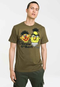 Olive green cotton t-shirt featuring a graphic print of two cartoon characters with vibrant colors, round faces, and playful expressions.