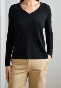 Svart långärmad tröja med V-halsdesign och ribbade muddar, tillverkad av mjukt material, kombinerad med ljusa byxor.