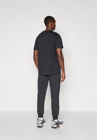 Melnā īsām piedurknēm t-kreklā, pelēkos sporta biksēs un melnbaltajās sporta apavos. T-kreklam ir taisna fasona; biksēm ir sašaurināti ieplokņu gali.