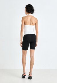 Bela oprijeta majica na vrat z odprtim hrbtnim delom, kombinirana s črnimi kolesarskimi hlačami, dopolnjena z odprtimi črnimi petami. Gladek material s preprostim, krojenim dizajnom.