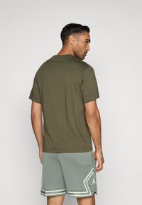 Λαδί κοντομάνικο t-shirt με χαλαρή εφαρμογή, συνδυασμένο με ανοιχτό γκρι κοντές σορτς από πλέγμα, που διαθέτουν λογότυπο διαμαντιού και ρίγες.