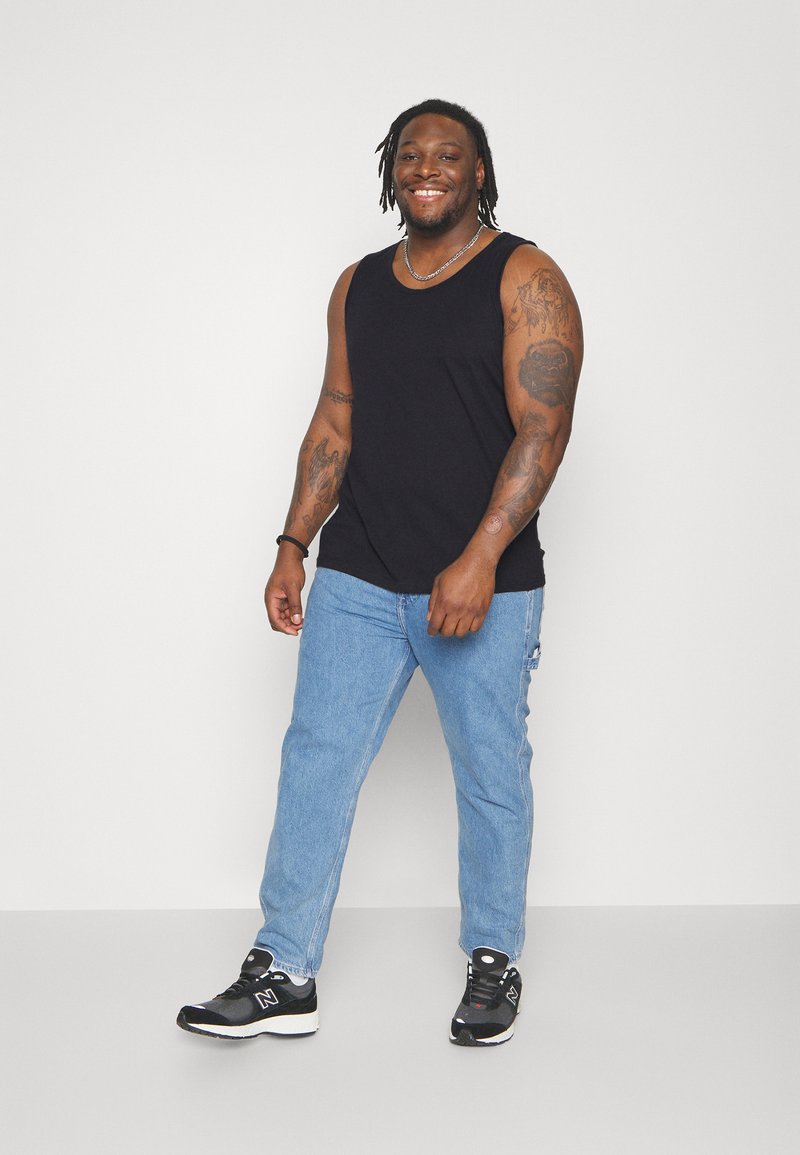 Canotta nera senza maniche, jeans in denim blu e sneakers nere. La canotta è in cotone; i jeans hanno una vestibilità rilassata con lievi segni di usura.