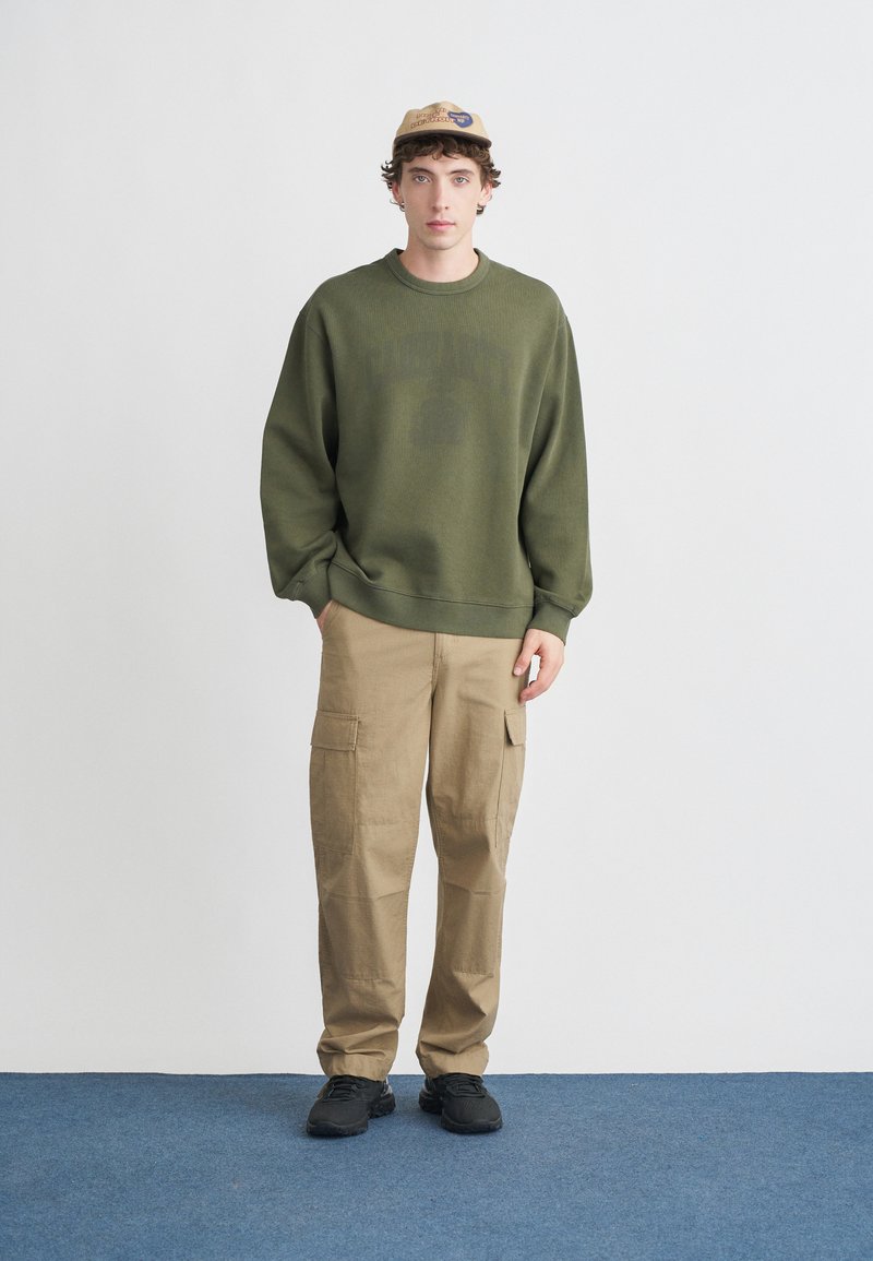 Green sweatshirt, beige cargo pants, and black sneakers. Sweater features ribbed cuffs and hem, relaxed fit. Structured cap with logo.