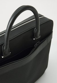 Valigetta nera con texture, dotata di doppio manico, chiusura con zip metallica e tasca esterna con foderatura liscia.