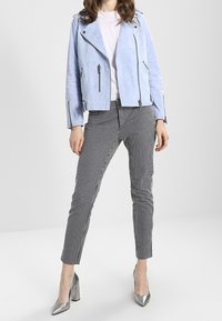 Giacca da moto in finta suede blu chiaro, pantaloni a righe nere e bianche e tacchi alti argentati. T-shirt semplice indossata sotto.