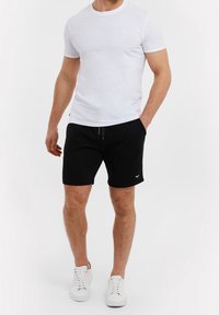 T-shirt en coton blanc associé à un short noir. Le short dispose d'une taille à cordon et d'un petit détail de logo. Des baskets blanches complètent la tenue.