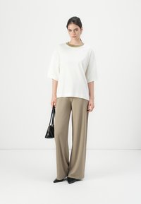 Witte oversized t-shirt met groene kraag, gecombineerd met brede beige broek. Model houdt een kleine zwarte tas vast; schoenen zijn zwarte puntige.