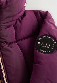 Veste matelassée violette avec texture quiltée, un patch de marque avec "BAKER" en noir et or, et une fermeture éclair en or rose.
