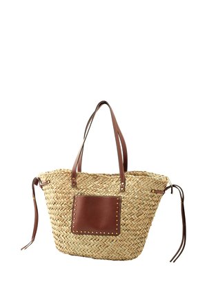 Bolso tote de paja tejido con dos asas de cuero marrón, un bolsillo frontal de cuero marrón con tachuelas de bronce y cordones laterales ajustables.