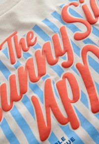 Close-up van crèmekleurige stof met verhoogde koraalrode tekst in schrift over lichtblauwe verticale strepen.