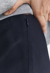Navy trousers with a textured finish and a side zipper detail, paired with a gray pullover, showcasing a close-up view of fabric and design.