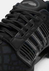 Must sportlik jalanõu, millel on mustriline tekstiilist pealmine osa, läikivad plastdetailid ja tekstuuriga paelad kindlaks kinnitamiseks.
