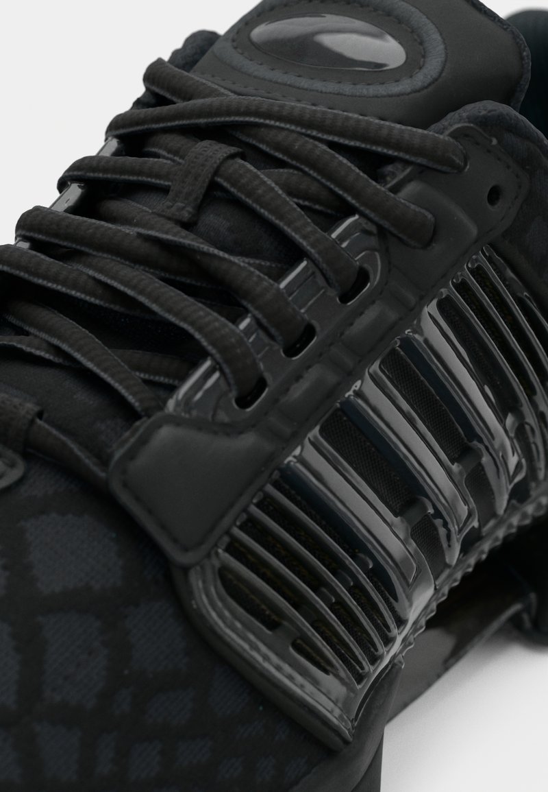 Sort atletik sko med mønstret tekstiloverdel, blanke plastikdetaljer og teksturerede snørebånd for en sikker pasform.