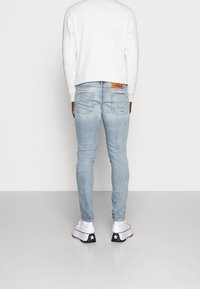 Vaqueros de mezclilla azul claro con un ajuste slim, con detalles desgastados y bolsillos traseros. Combinados con zapatillas blancas y una sudadera gris.