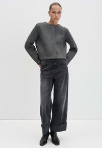 Giacca grigia cropped con finitura testurizzata, abbinata a jeans in denim neri a gamba larga con vita alta e stivali neri con punta a punta.