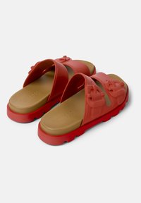 Red rubber slide sandals with two wide straps, featuring molded details and a tan footbed. Chunky sole with grip texture.