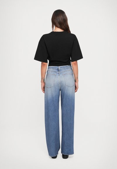 Svart kortermet topp kombinert med lyseblå, vide jeans med en gradientdesign og baklommer. Glatt stofftekstur.