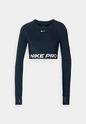 Melnā sporta krekla ar garām piedurknēm, īsā dizainā, izgatavots no elastīga materiāla, ar "NIKE PRO" tekstu baltā krāsā apakšmalā un pirkstu caurumiem piedurknēs.