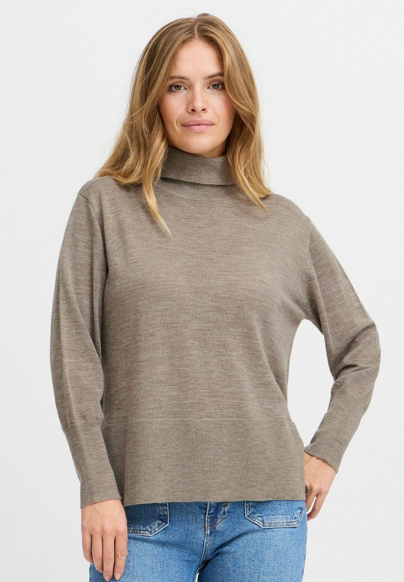 Pull à col roulé marron avec une coupe décontractée et des manches longues, présentant une texture à côtes fines et un ourlet droit, associé à un jean bleu.