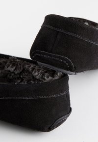 Svarta tofflor i mocka med en mjuk, luddfylld insida. Har förstärkt sömnad och en låg profil i gummi under sulan. Klassisk, enkel design.