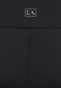 Schwarze Sportleggings mit einer glatten Textur, minimalen Nähten und einem kleinen grauen "LA"-Logo am Bund.