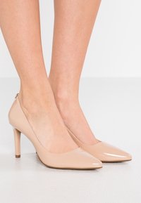 Escarpins à talons hauts en cuir verni beige, avec un bout pointu, un talon élancé et un design minimaliste. Texture lisse avec un éclat subtil.