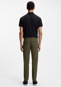 Czarna teksturowana koszulka polo z krótkimi rękawami, w zestawieniu z oliwkowozielonymi spodniami z tylnymi kieszeniami i dopasowanym krojem. Całość uzupełniają czarne trampki.