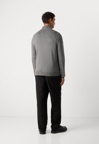 Gray knit sweater with a mock collar, slim fit, and long sleeves, paired with black trousers and black shoes. Smooth texture, subtle pattern.