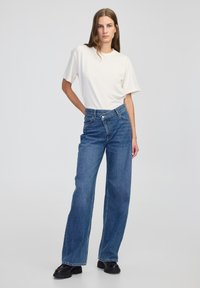 Witte t-shirt met korte mouwen gecombineerd met lichtblauwe hoge taille wijde jeans. Jeans hebben voorzakken en een knoopsluiting. Zwarte chunky laarzen.