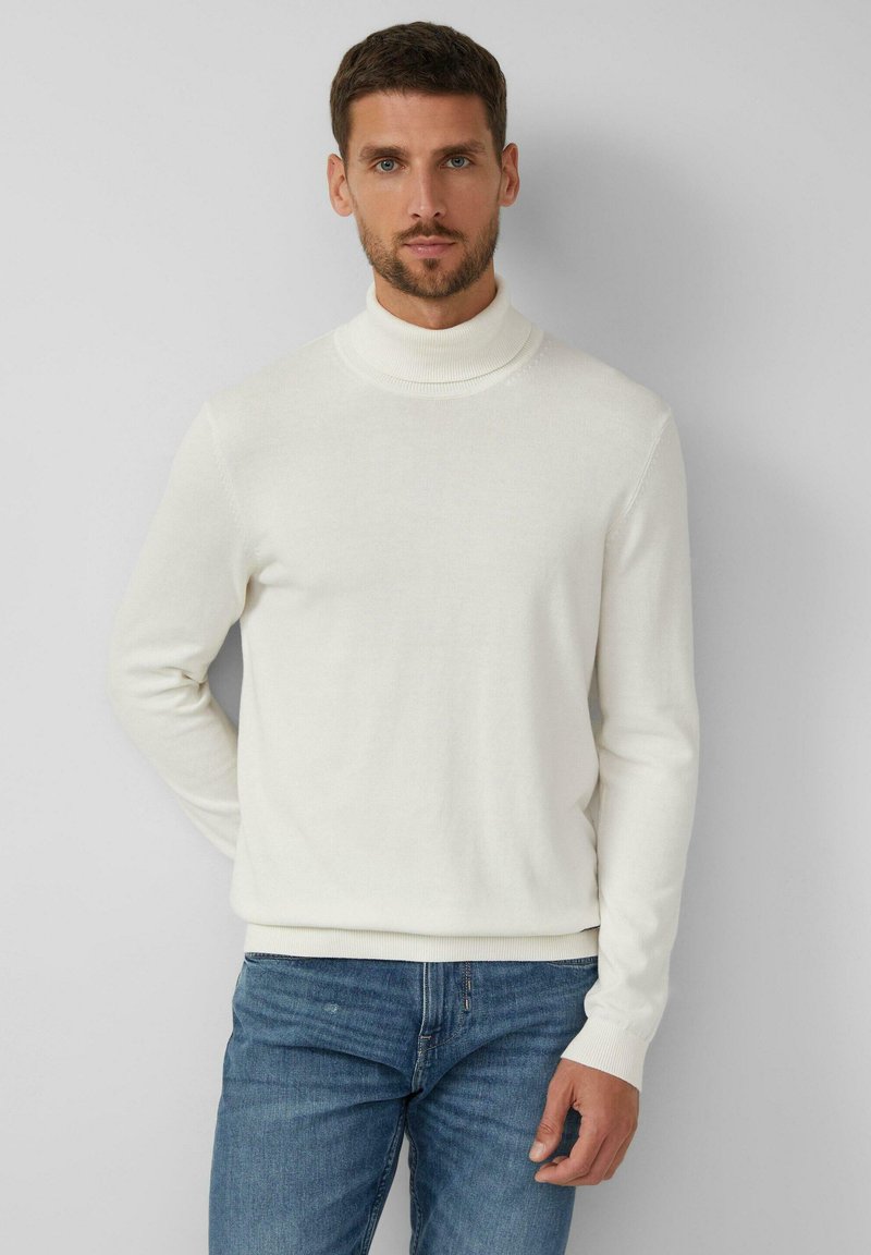 Weißer Rollkragenpullover aus weichem Stoff, mit langen Ärmeln und gerippten Bündchen. Kombiniert mit blauen Jeans.