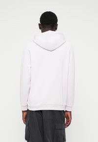 Ανοιχτό μωβ φούτερ με λεπτομέρεια στον λαιμό και την κουκούλα, με μακριά μανίκια και ριμπ ένωμα, φορεμένο πάνω από σκούρες cargo παντελόνες.