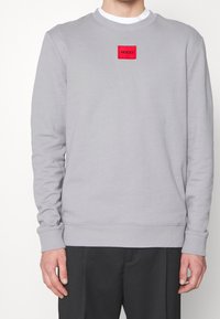 Sudadera gris hecha de una mezcla de algodón, con mangas largas, puños de canalé y un parche de logo rectangular rojo en el pecho.