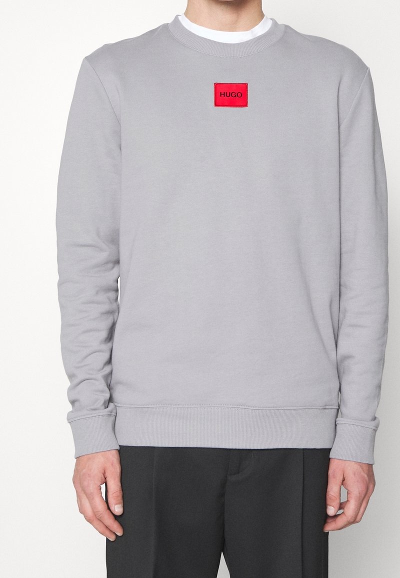 Sudadera gris hecha de una mezcla de algodón, con mangas largas, puños de canalé y un parche de logo rectangular rojo en el pecho.