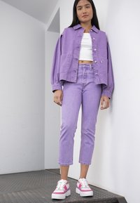 Jaqueta de ganga roxa sobre uma t-shirt cropped branca, combinada com calças de ganga roxas e ténis com detalhes em rosa. Textura suave e corte descontraído.