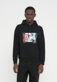 Melns kokvilnas džemperis ar kapuci, kam priekšpusē grafiskais attēls ar sarkaniem, baltiem un ziliem krāsu blokiem un komiksu stila ilustrācijām. Aprīkots ar kenguru kabatu.